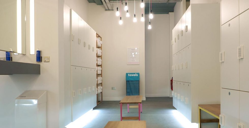 Locker room with white laminate lockers, towel racks, benches and mirrors at Soul Cycle.