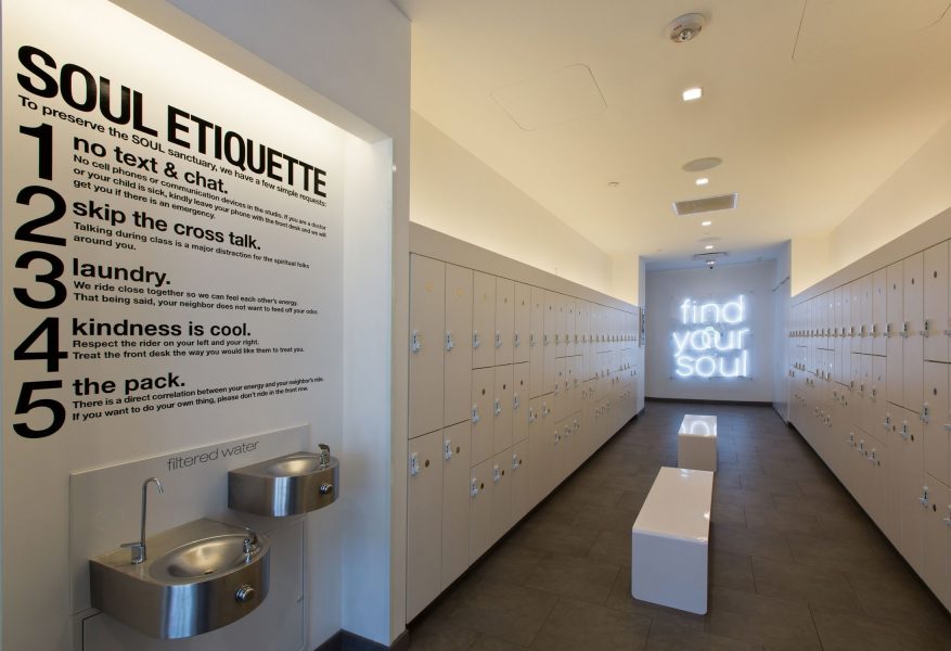 Long hallway with different models of white laminate lockers and a neon sign at Soul Cycle.
